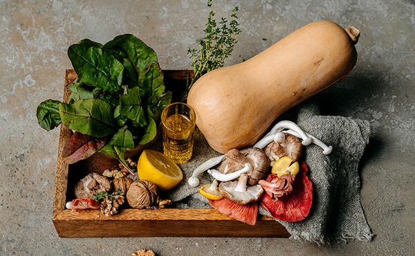 Colourful produce for a hearty vegan dinner including butternut squash, mushrooms, leafy greens and walnuts in a rustic tray.